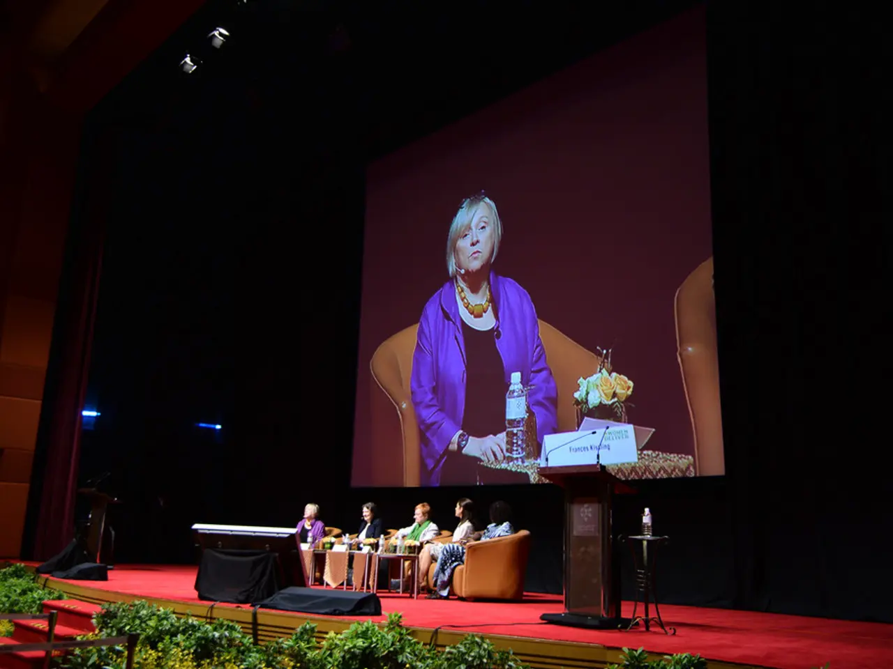 In this image, we can see some people sitting on the sofas, there is a red color carpet, we can see...