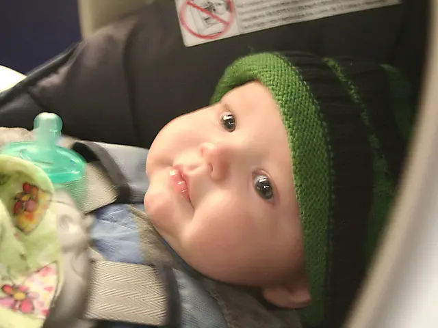 In this image I can see a baby and he is wearing a cap. I can also see a handkerchief and a bottle.