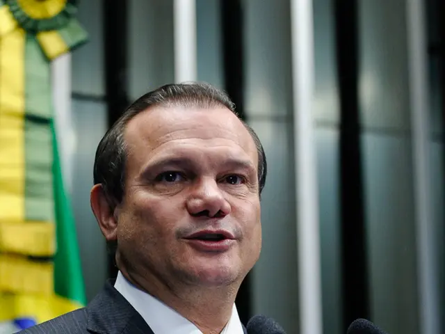 In this image there is a man standing on the stage and speaking in a microphone.